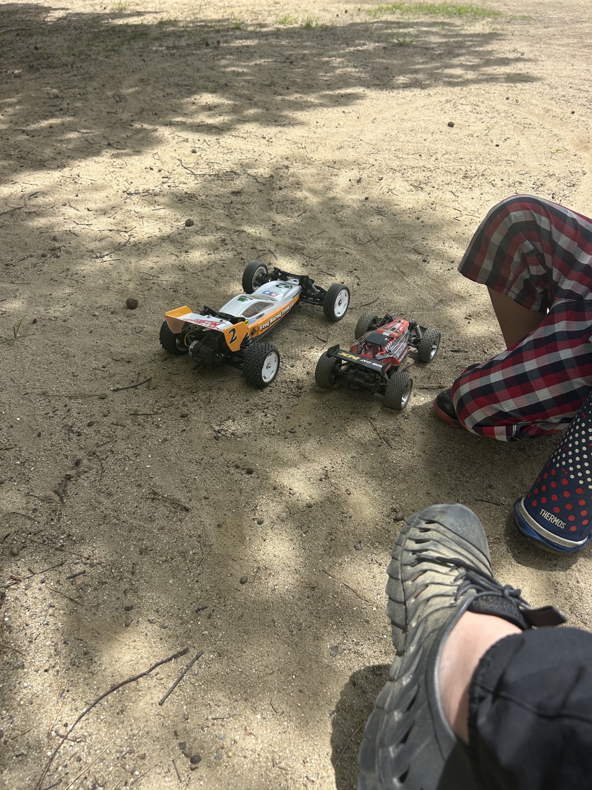 土の上で子どものそばに並ぶ黄色いバギーと赤いRCカー